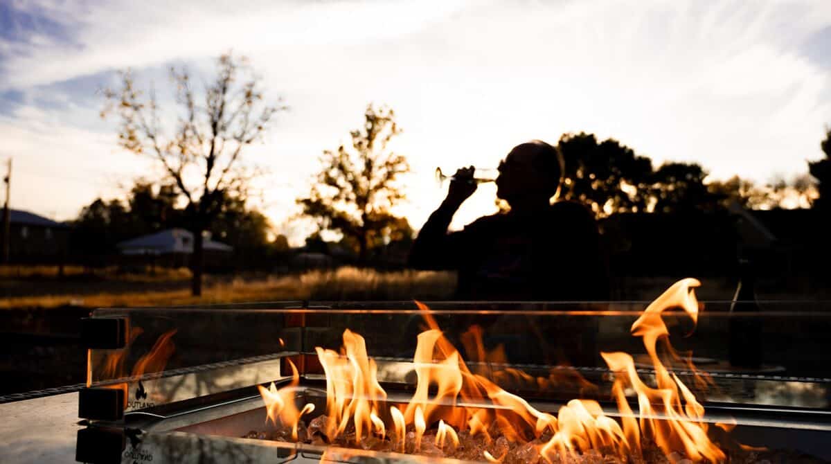 a fire pit at dusk with fire dancing and the silouette of a person in the background drining a glass of wine