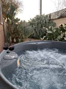 Hot tub with a background of prickly pear cacti. Two wine glasses with red wine are on the sie f the hot tub.