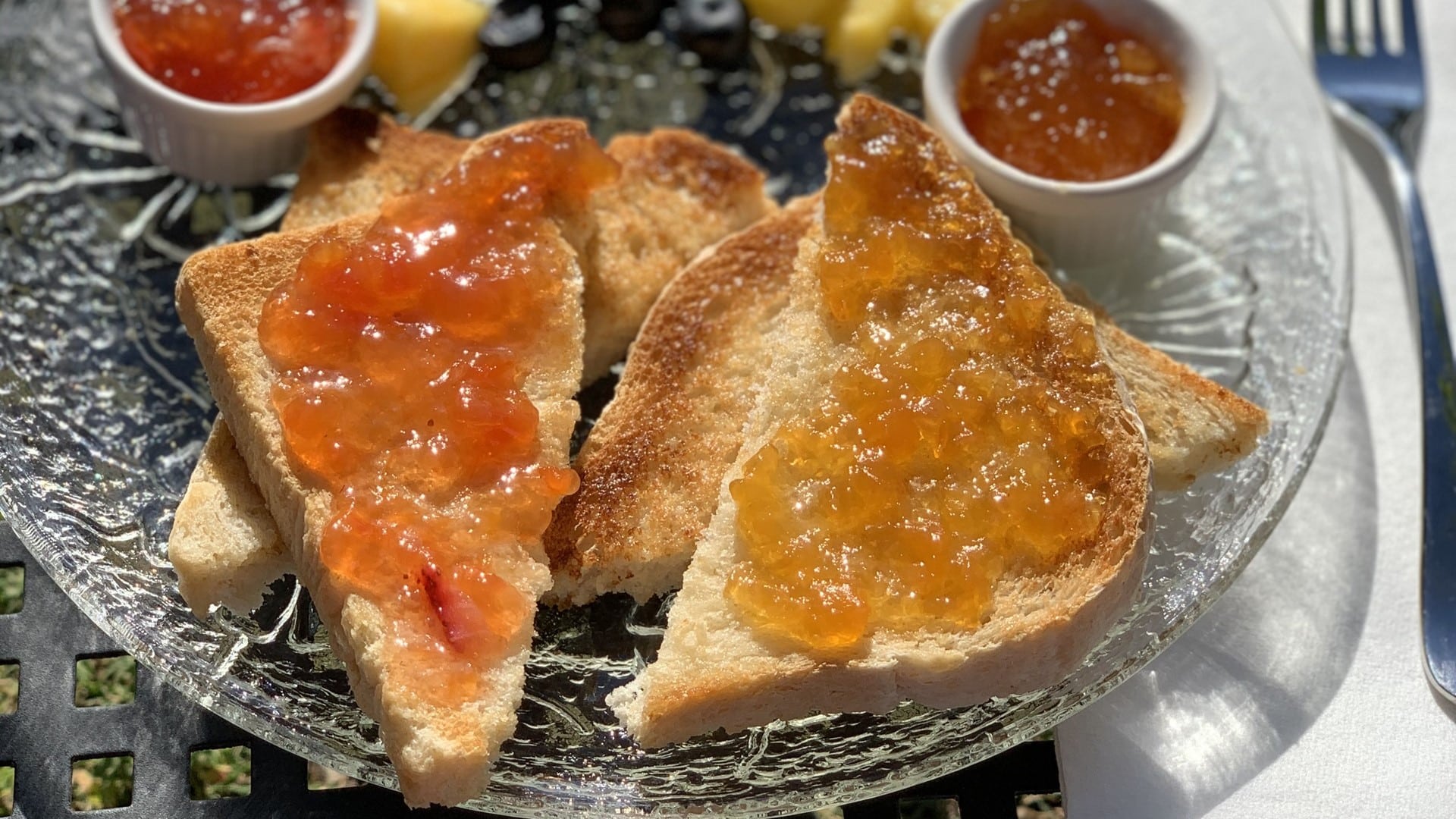 Toast with colorful jams and some fruit in the background