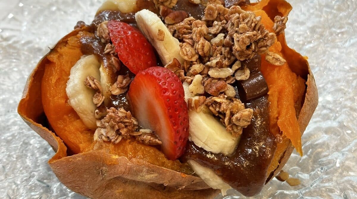 a baked sweet potato with strawberries, bananas, almond butter, maple syrup and granola