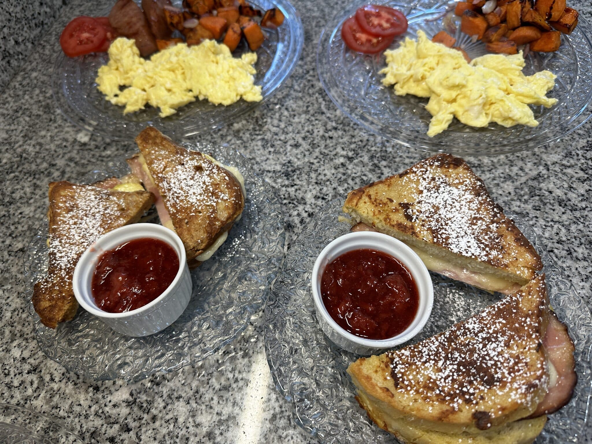 French toast dusted in powdered sugar, jam, scrambled eggs, tomatoes