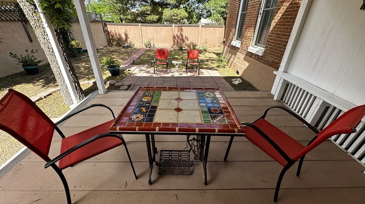 a patio with red chairs and a tile table between them looking out over a garden with more chairs and grass
