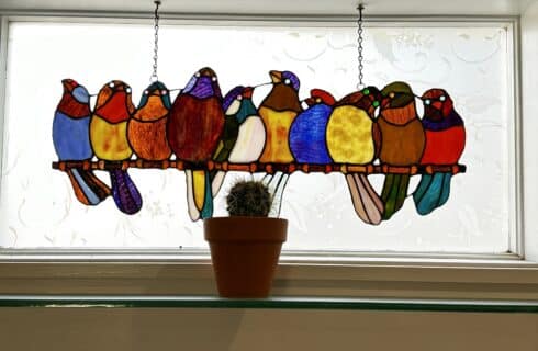 Stained glass birds in front of a window with a potted cactus in front