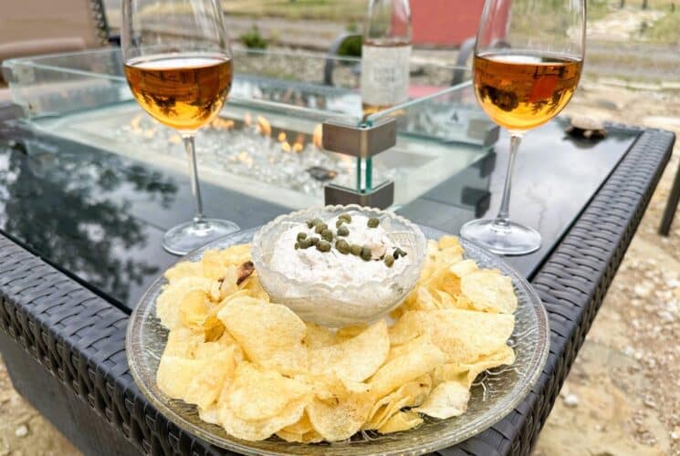 potato chips on a plate surrounding a bowl of dip. The plate is on a lit fire pit with two glasses of rose wine and a bottle of wine in the background.