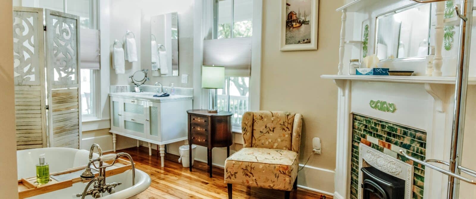 elegant bathroom with an antique clawfoot soaking tub, fireplace, vanity, windows, and wood floor