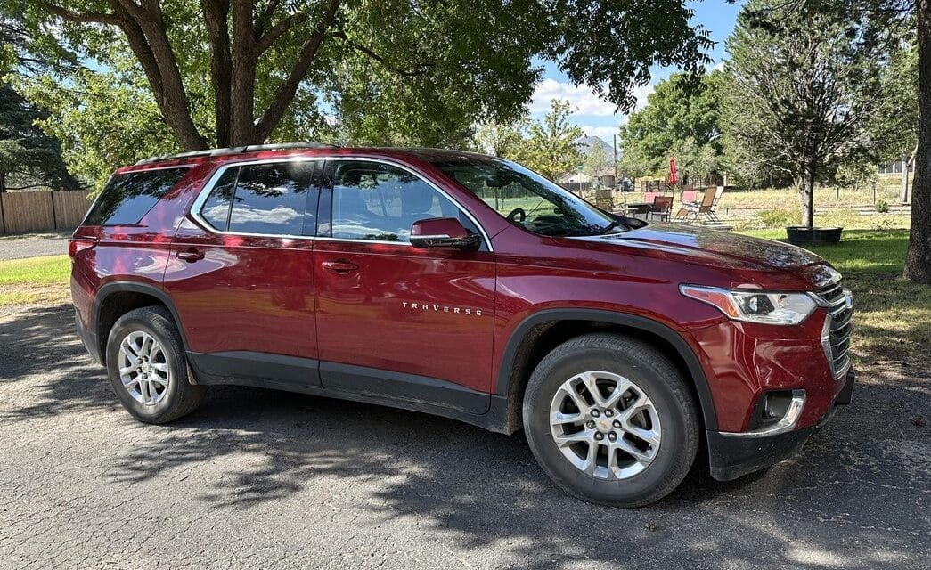 A red Chevy Traverse SUV in a driveway, with trees and a fire pit behind it.