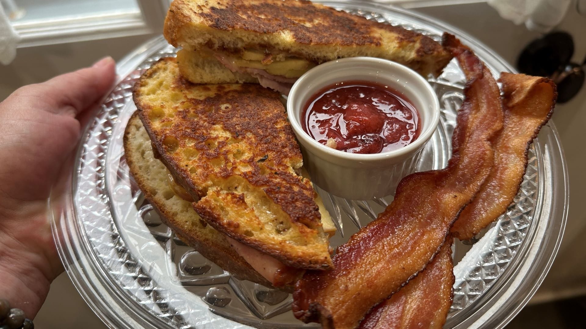 a grilled sandwich with a fruit compote on the side and two slices of bacon