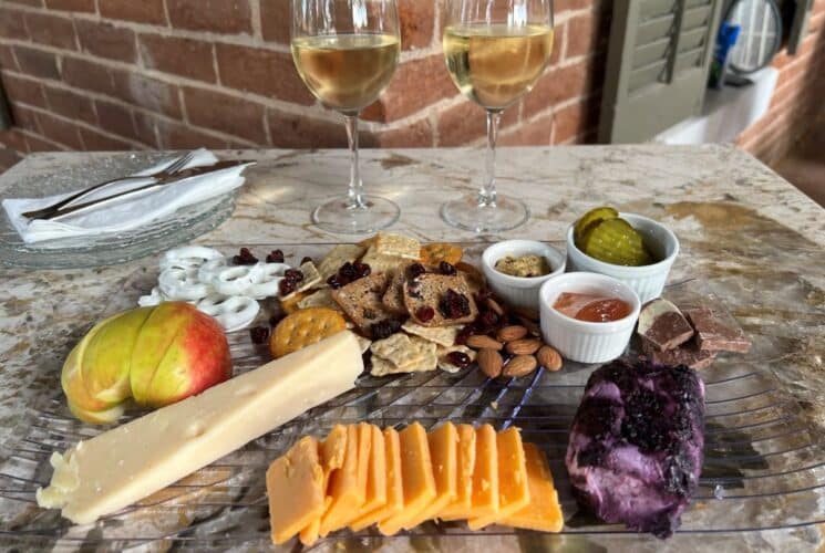 Cheese tray with 3 cheeses, crackers, apples, pickles, wine, and other items