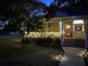 A front porch lit in warm light, with a wreath on the door and lights across the banister