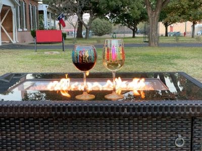 a fire pit with fire and two colorful wine glasses sitting on it, one with white wine and one with red wine.